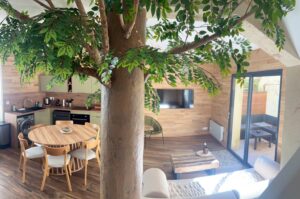 Salon avec arbre intégré dans une maison cabane à Cholet, cuisine ouverte et terrasse