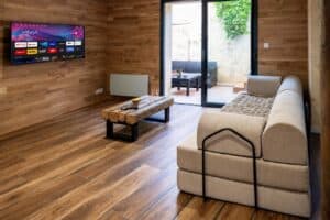 Salon chaleureux en bois de la Maison Cabane à Cholet avec canapé, télévision murale, table basse rustique et accès à la terrasse.